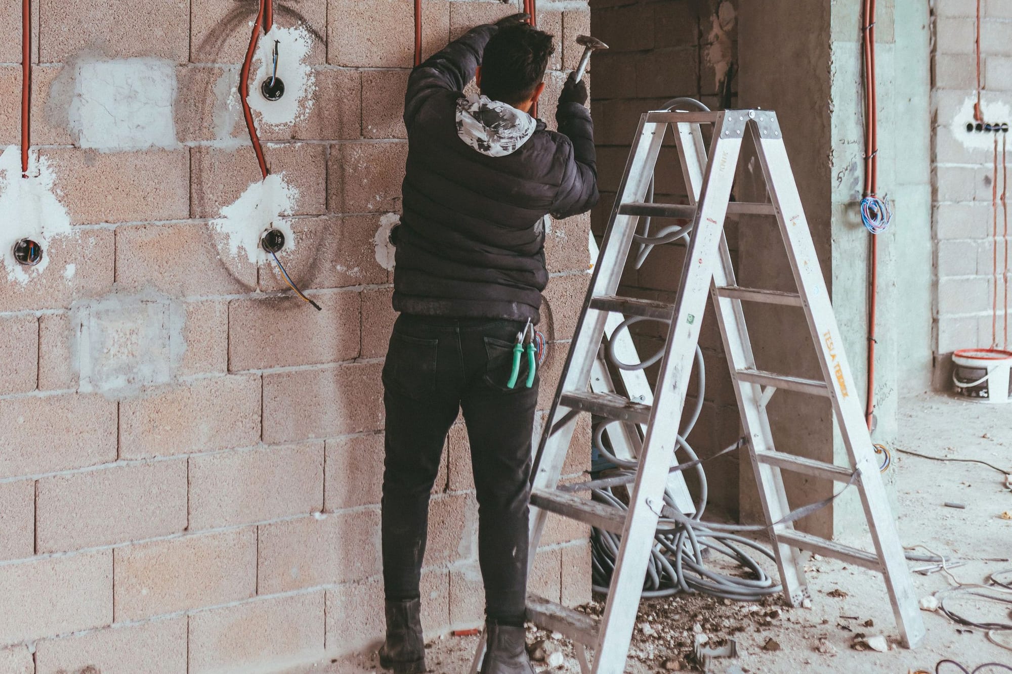 Monteur setzt Leerrohre in eine Ziegelwand im Rohbau, daneben eine Leiter.