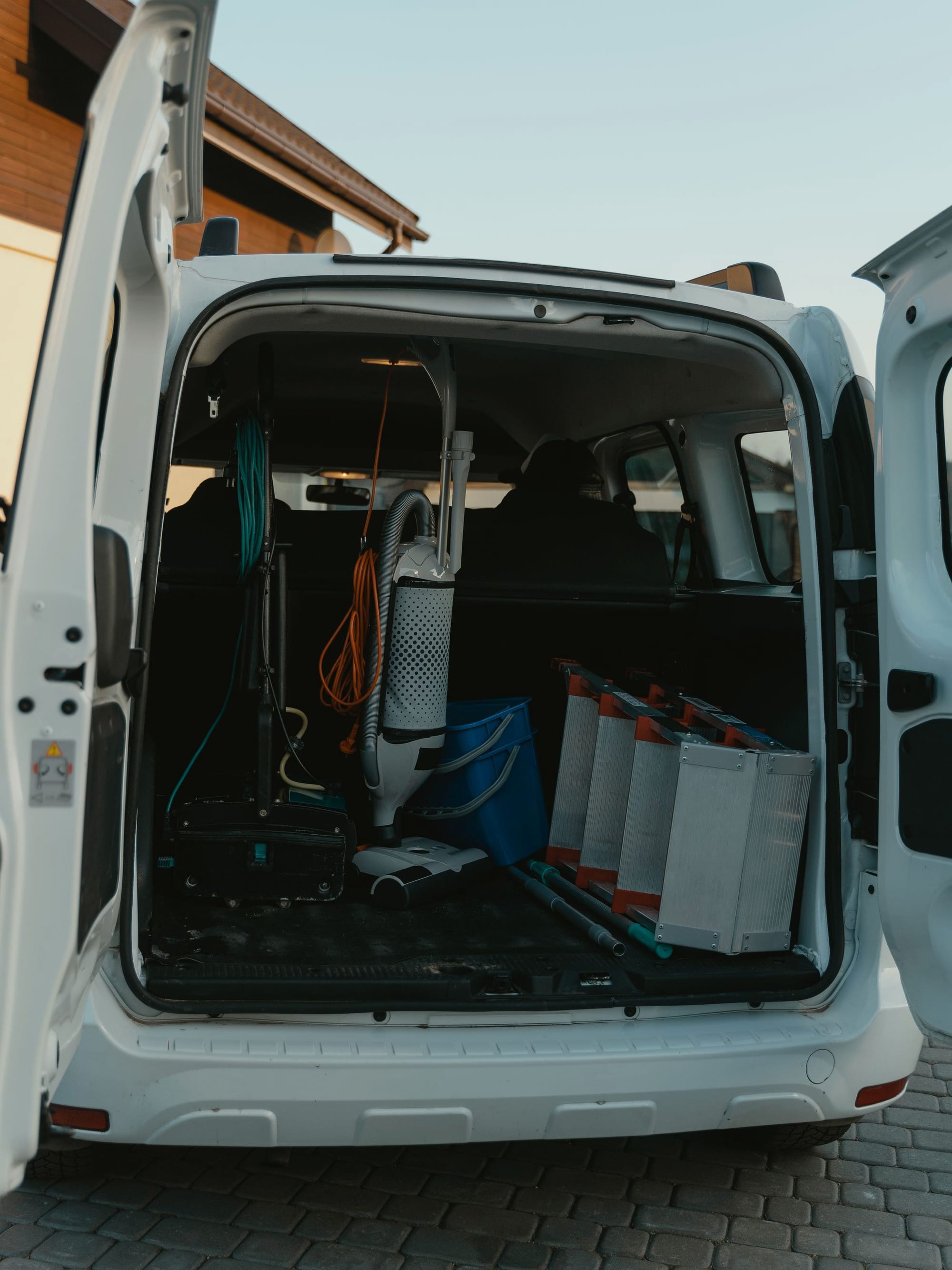 Offene Hecktür eines Transporters mit Reinigungsgerät und Kisten auf Pflaster.